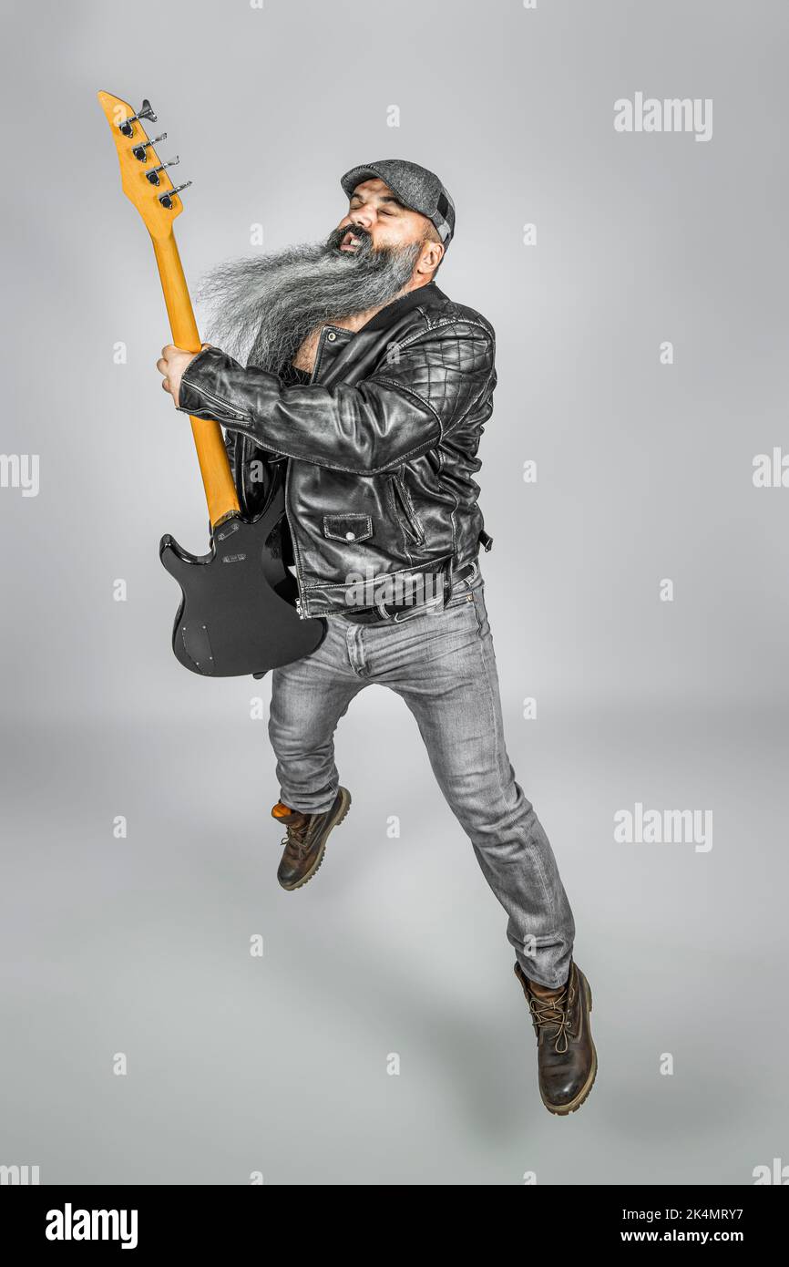 Rocker mit Gitarre und langem Bart, der während des Spielens einen Sprung durchführt Stockfoto