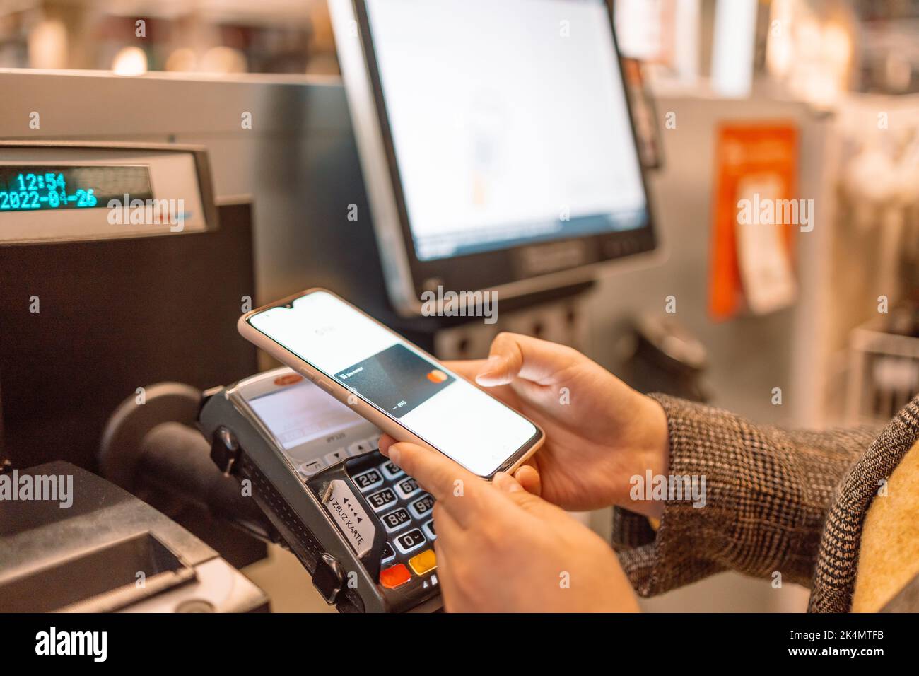 Krakau, Polen – 26. April 2022: Seitenansicht der jungen Frau, die beim Selbstabmeldung mit der Smartphone-App im Geschäft bezahlt Stockfoto