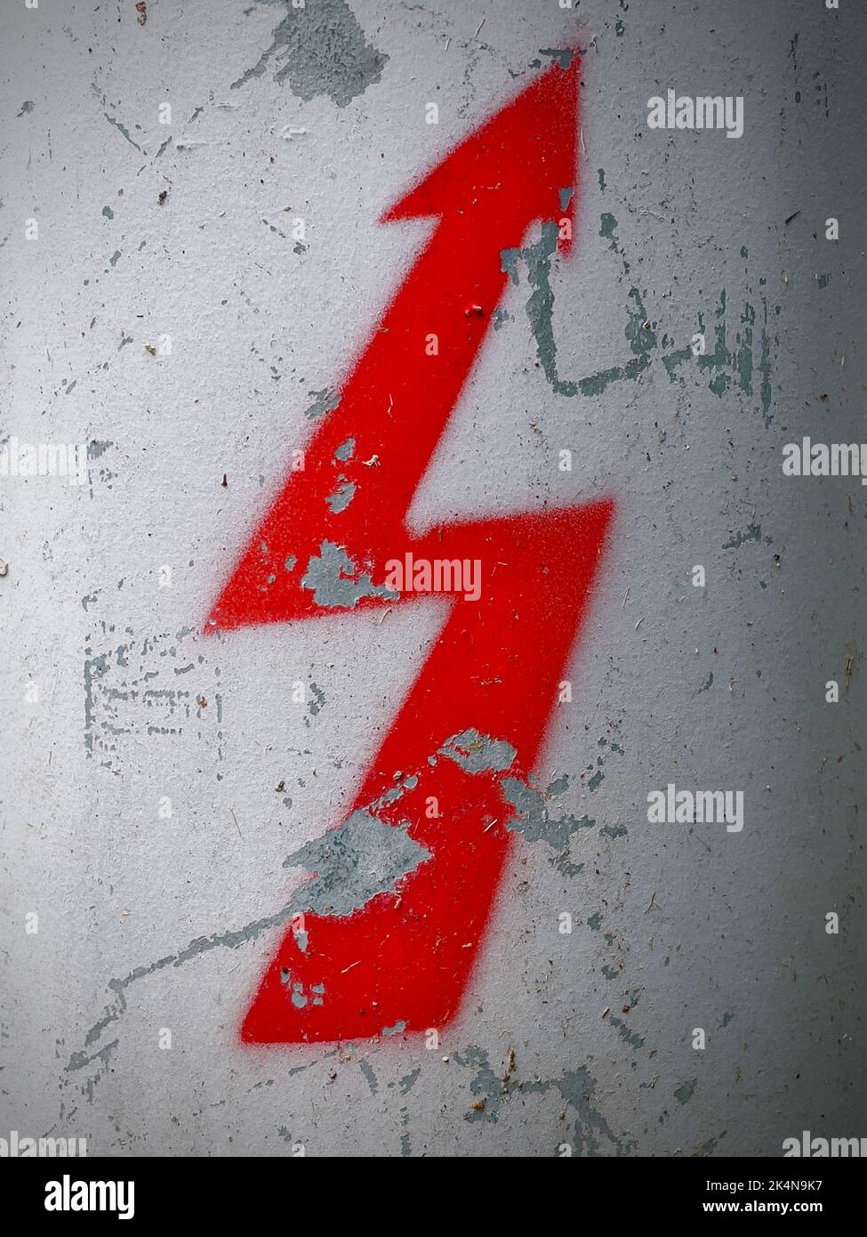 Ein rot gestrichenes Blitzsymbol, das auf eine verwitterte Wand gezeichnet ist Stockfoto