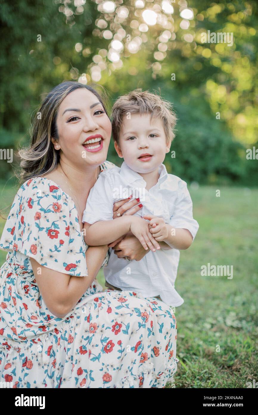 Die asiatische Mutter kniet neben ihrem 2-jährigen Sohn und lächelt. Stockfoto