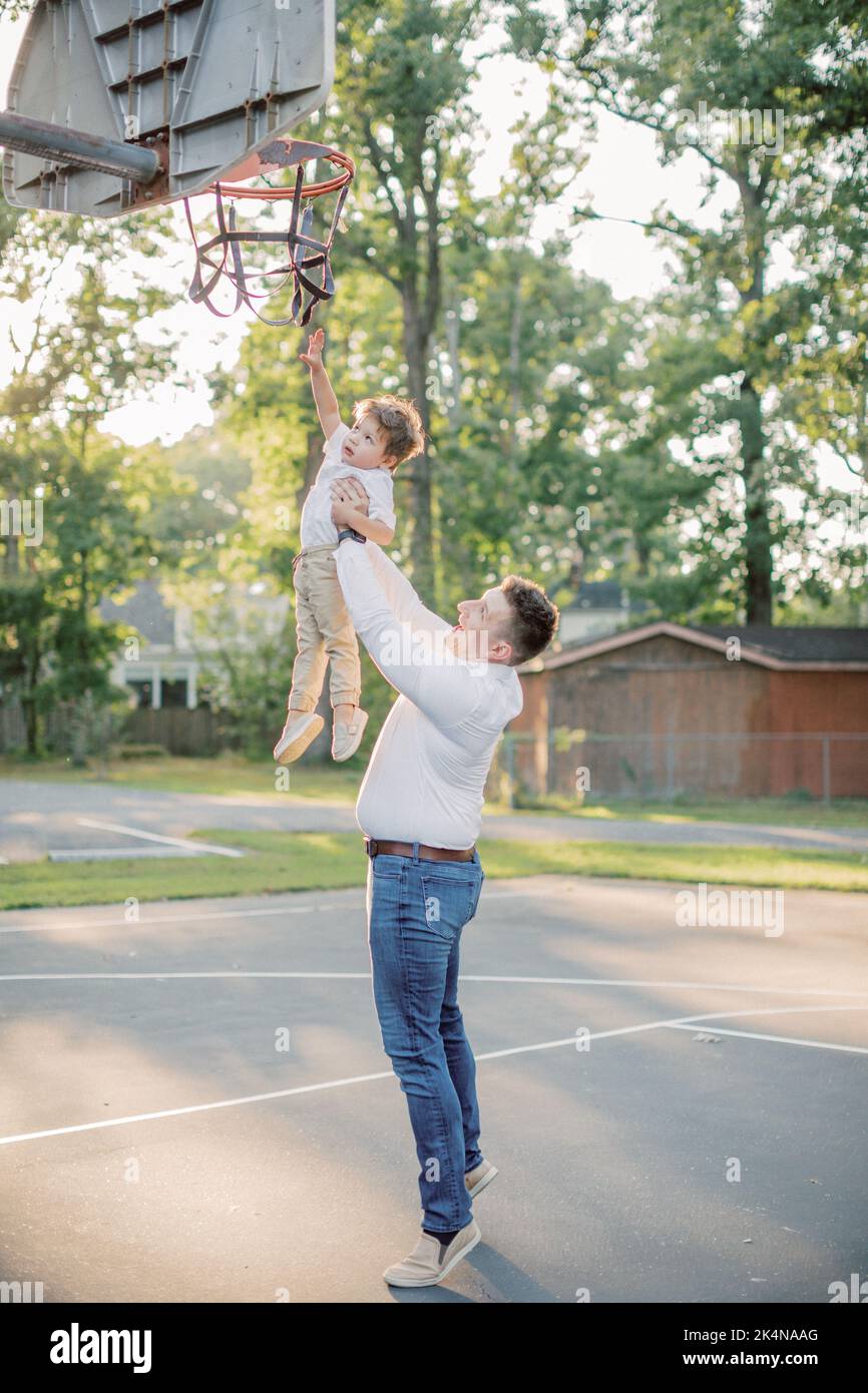 Der kaukasische Vater hält einen 2-jährigen Sohn bis zum Basketballkorb. Stockfoto