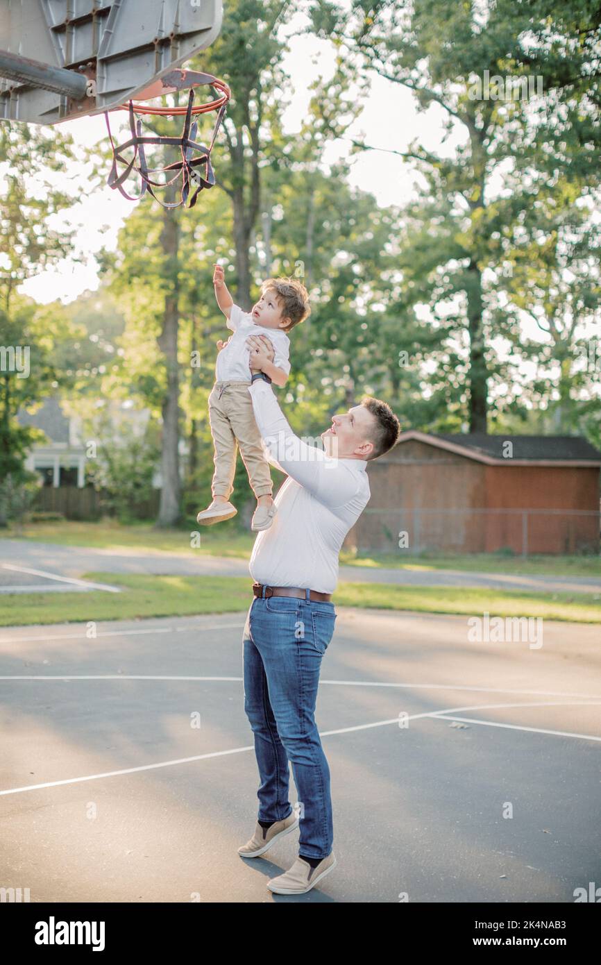 Der 30-35-jährige Vater hebt seinen 2-jährigen Sohn ins Basketballnetz. Stockfoto