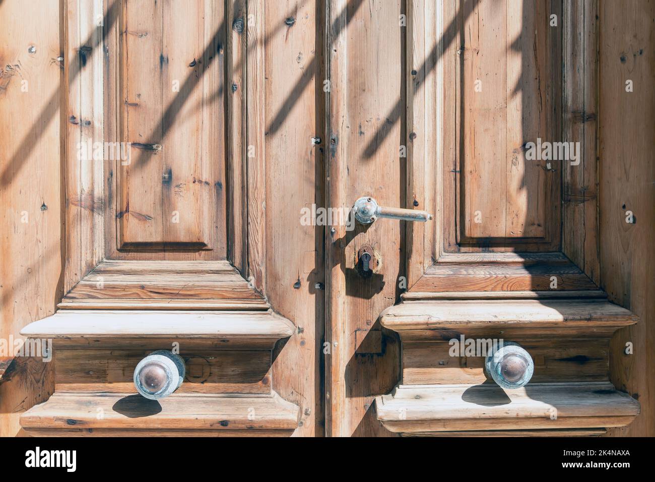 Hölzerner brauner geschlossener Türhintergrund. Vintage Eingang mit Metallgriffen, Knopf, Schlüsselloch. Traditioneller griechischer Inselbau, sonniger Tag. Stockfoto