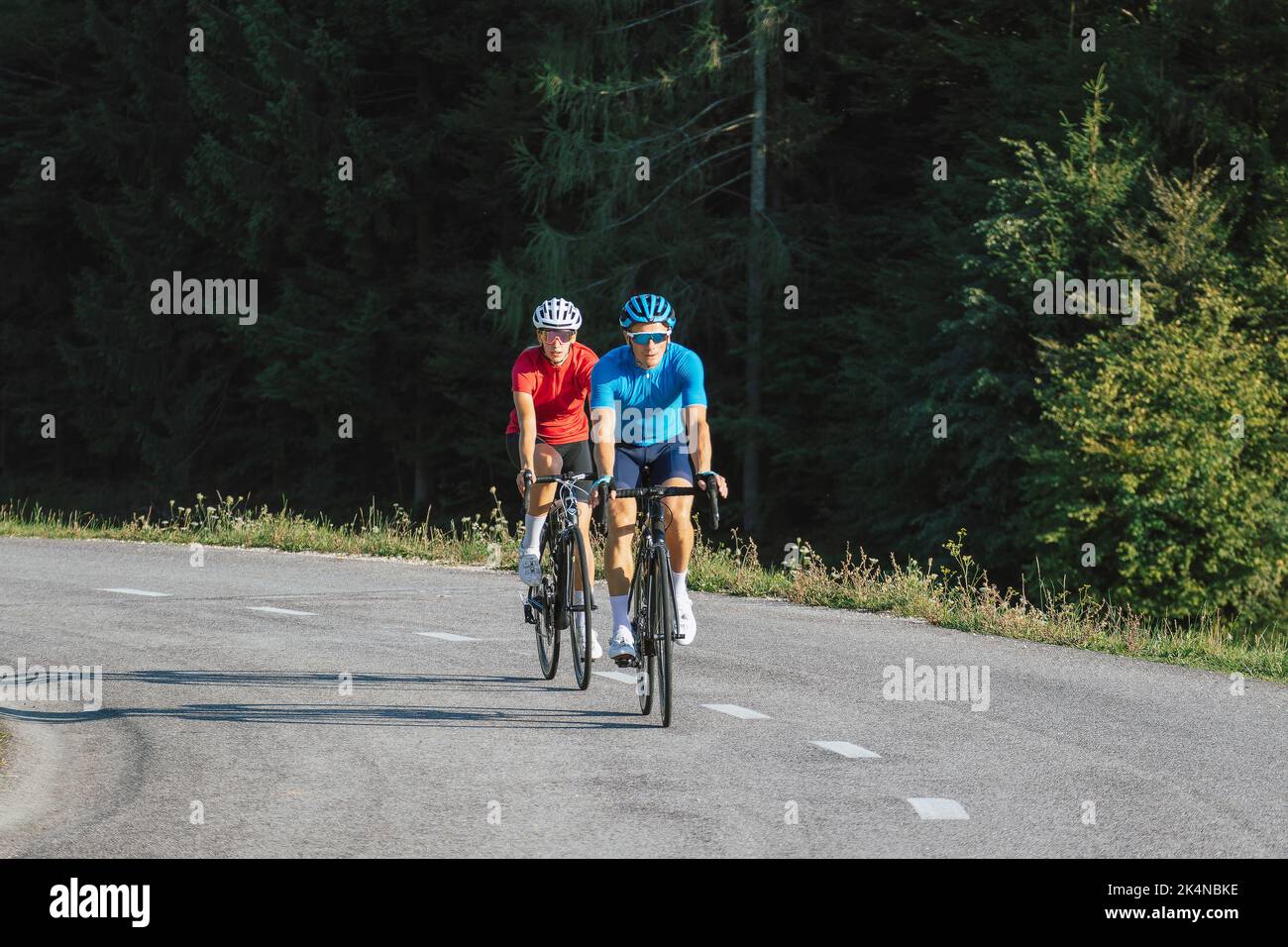 Der professionelle Rennradfahrer paart sich in Sporttrikots, trägt Fahrradhelme und Sonnenbrillen, die auf einer asphaltierten Straße treten Stockfoto