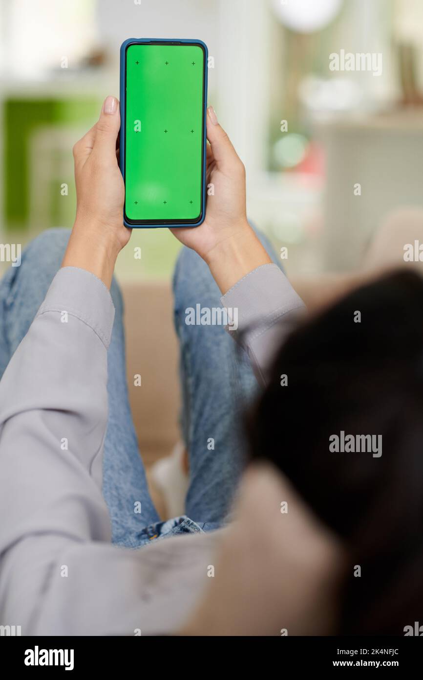 Leerer grüner Bildschirm des Smartphones in den Händen einer jungen Frau in der Casualwear, die vor der Kamera sitzt und Anwendung verwendet Stockfoto