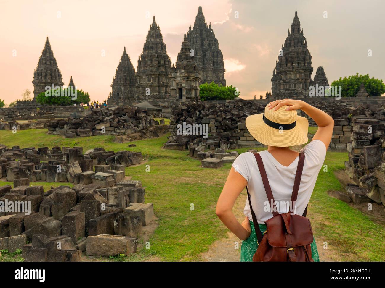 Frau, die während des Sonnenuntergangs auf ein Wahrzeichen am Prambanan Tempel schaut. Asiatische Frau mit weißem Kleid und Hut. Stockfoto