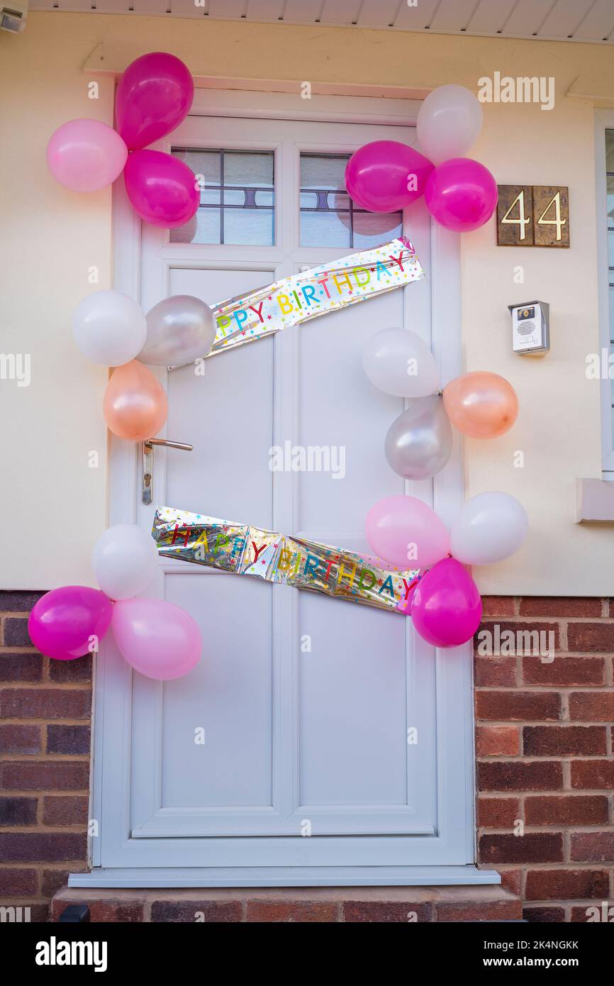 Happy Birthday Banner und Luftballons, die eine weiße, PVC-Vordertür einer britischen Wohnimmobilie schmücken. Feier von Geburtstagen. Stockfoto