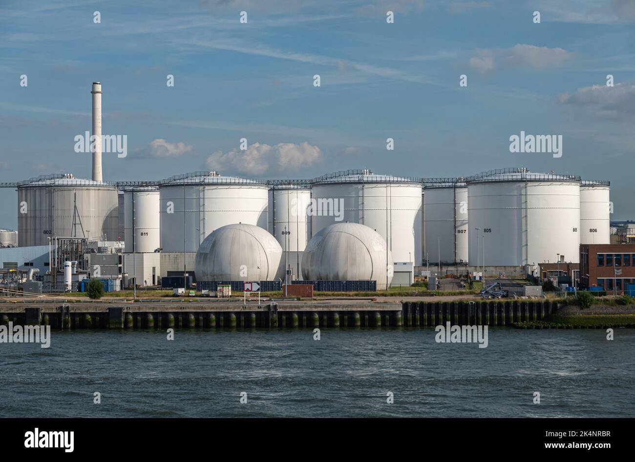 Rotterdam, Niederlande - 11. Juli 2022: Chevron White Oil and Gas Tanks under blue cloudscape with Red stone Office Building. Schornstein am Horizont Stockfoto