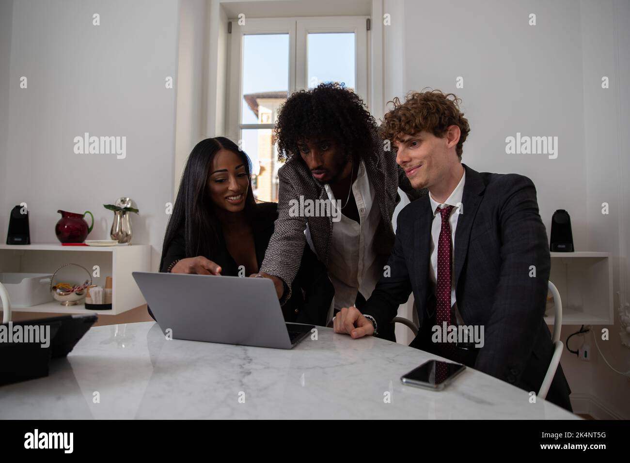 Eine Gruppe von drei Kollegen im Büro diskutiert ein Thema, arbeitet vor dem Computer. Stockfoto