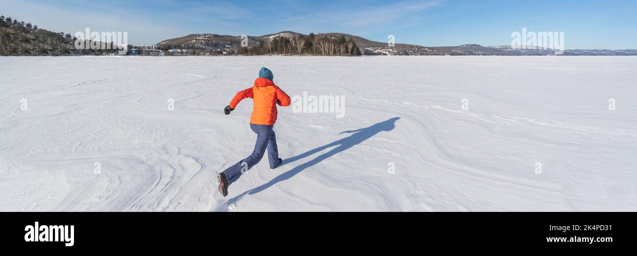 Frau, die auf einem gefrorenen See in einer verschneiten Winterlandschaft läuft. Winterspaß im Schnee. Panorama-Banner Stockfoto