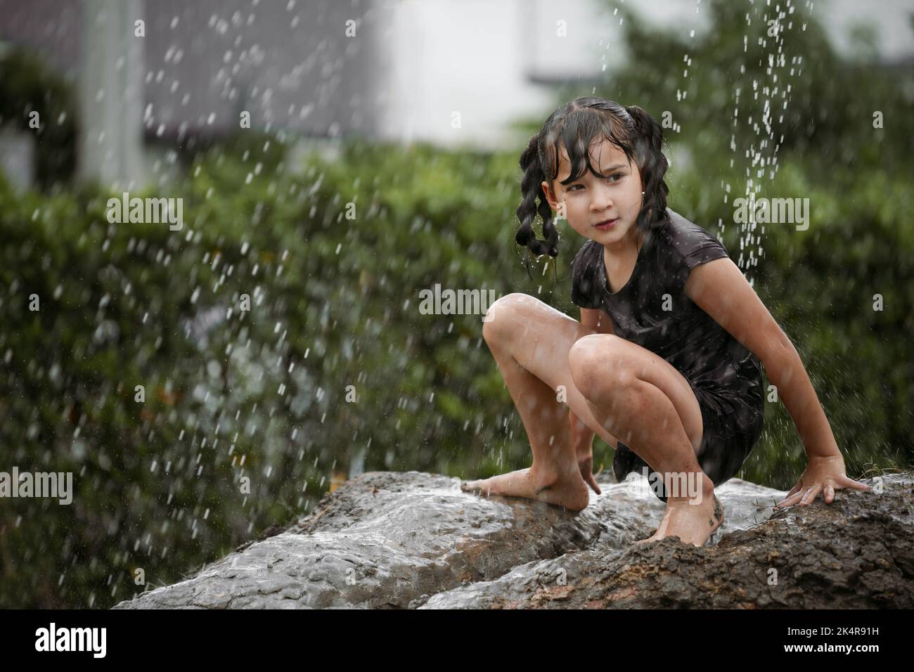 Fröhliches Kind Mädchen spielen auf Haufen von nassen Boden während der Regenzeit regnen. Stockfoto