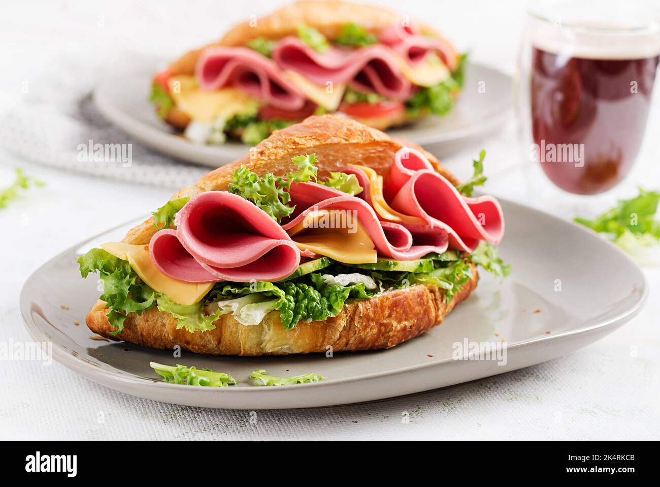Frisches Croissant oder Sandwich mit Salat, Schinken und Käse auf hellem Hintergrund. Stockfoto