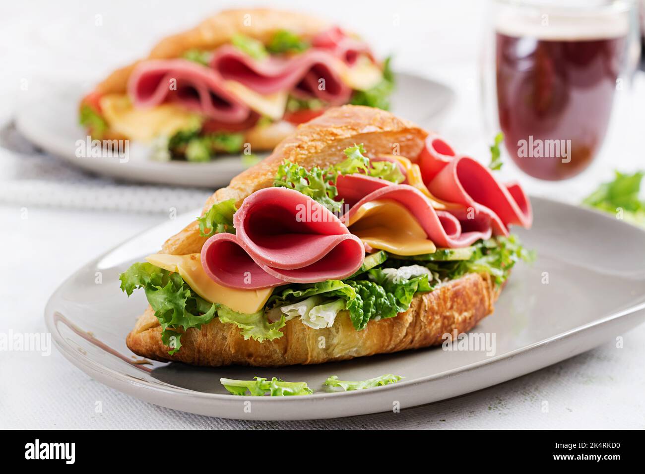 Frisches Croissant oder Sandwich mit Salat, Schinken und Käse auf hellem Hintergrund. Stockfoto