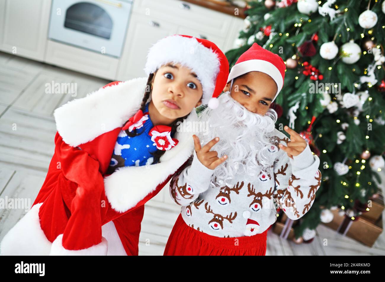 Afroamerikanische Kinder - Bruder und Schwester in einem großen weihnachtsmann Kostüm mit einem falschen Bartspiel und Grimasse vor dem Hintergrund der Weihnachten Stockfoto