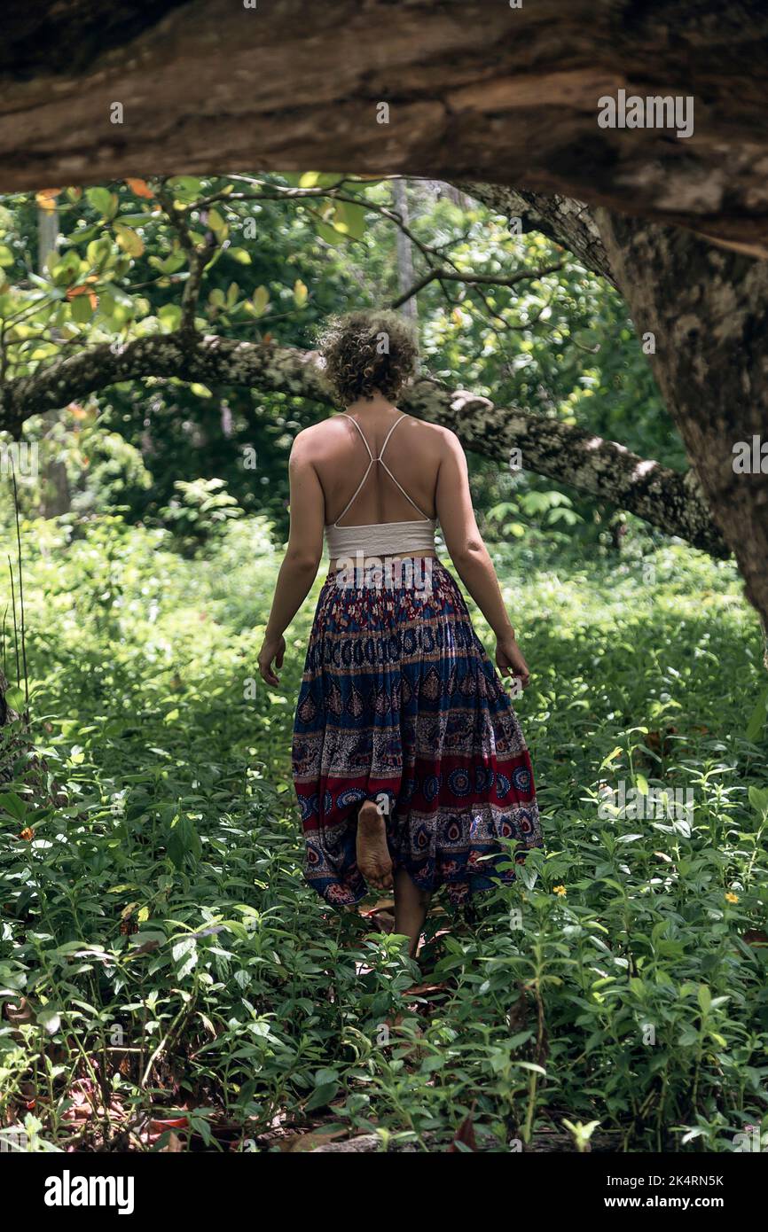 Kaukasische Frau mit blonden Haaren, gekleidet in ein weißes T-Shirt und einen langen Rock, der durch den Wald läuft. Sommerliche Stimmung Stockfoto