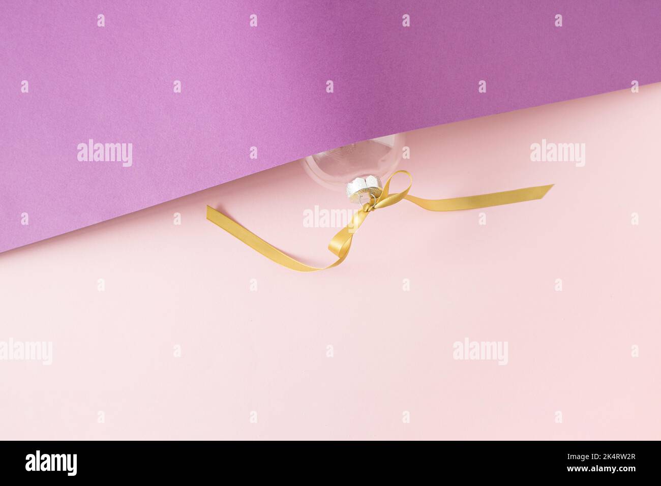 Weihnachtskugeldekoration mit goldenem Band auf violettem und pinkem Hintergrund mit Kopierraum. Neujahrskarte. Minimalistischer Style. Flach liegend. Stockfoto