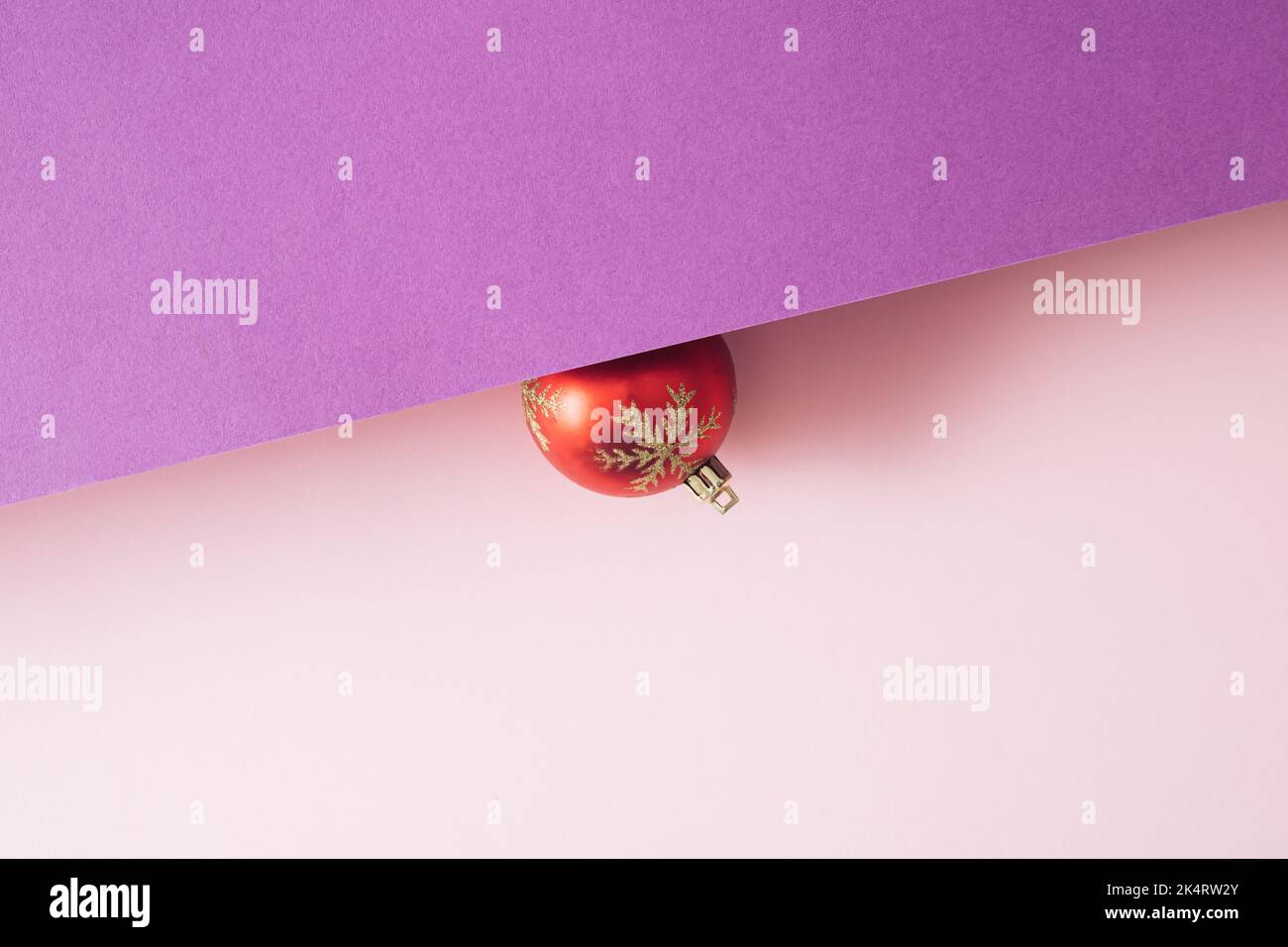 Rote Weihnachtskugel Dekoration mit auf lila und rosa Hintergrund mit Copy Space. Neujahrskarte. Minimalistischer Style. Flach liegend. Stockfoto