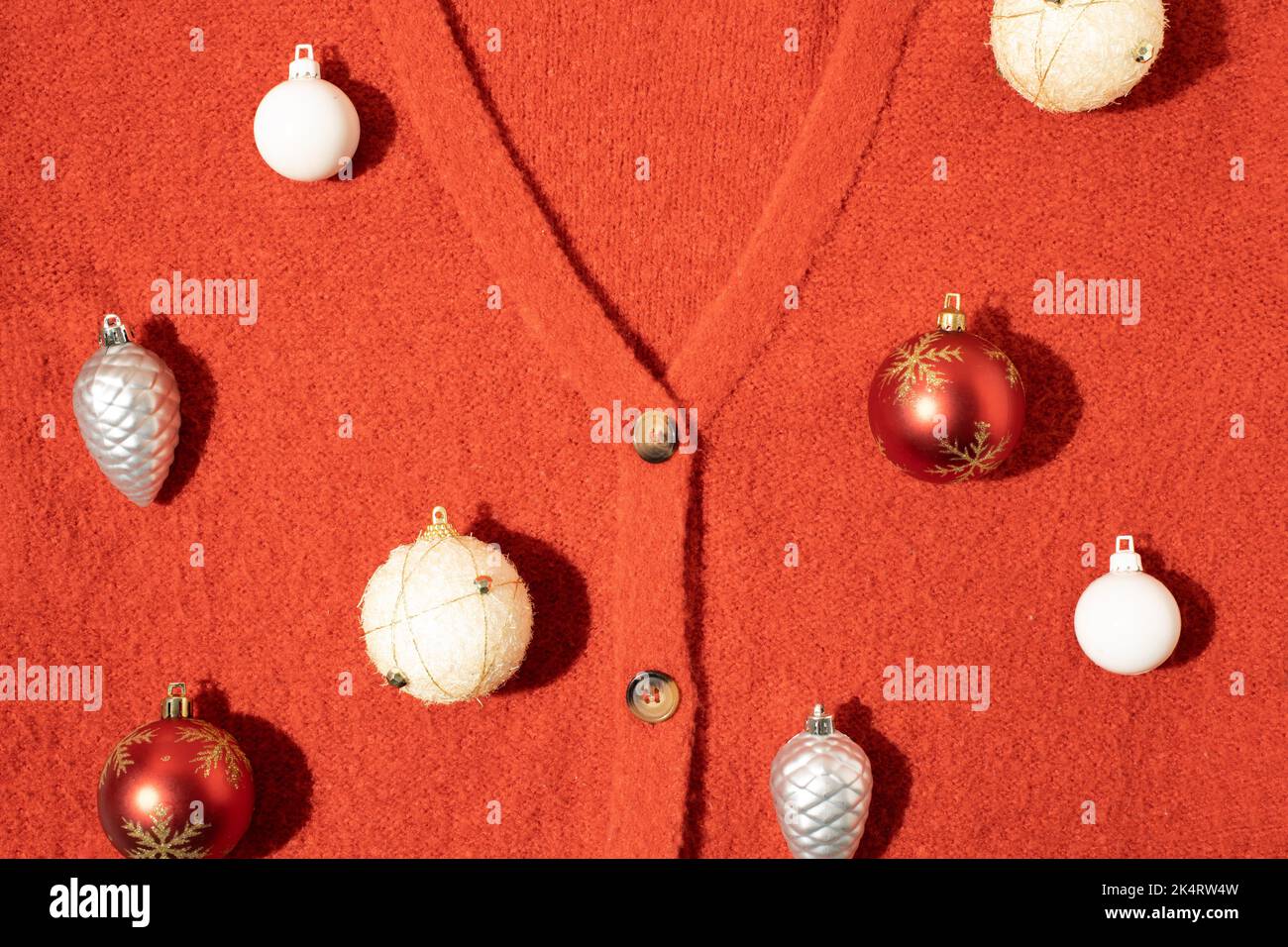 Weihnachtskugel-Dekoration auf rotem Strickpullover-Hintergrund. Neujahrskarte. Minimalistischer Style. Flach liegend. Stockfoto