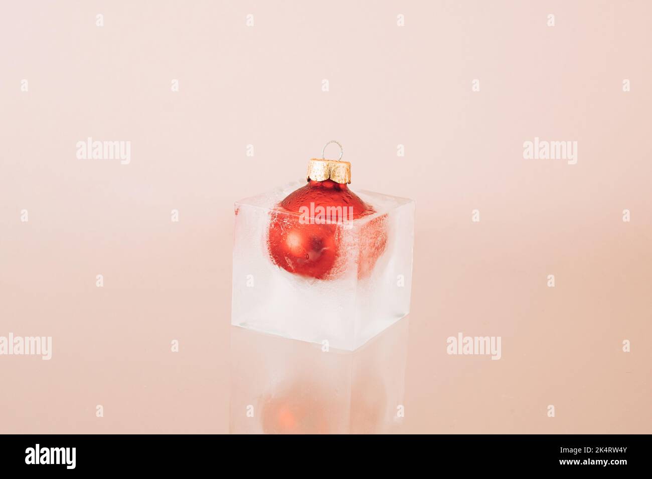 Rote Weihnachtskugel Dekoration eingefroren in Eiswürfel auf beigem Hintergrund. Neujahrskarte. Minimalistischer Style. Seitenansicht. Stockfoto
