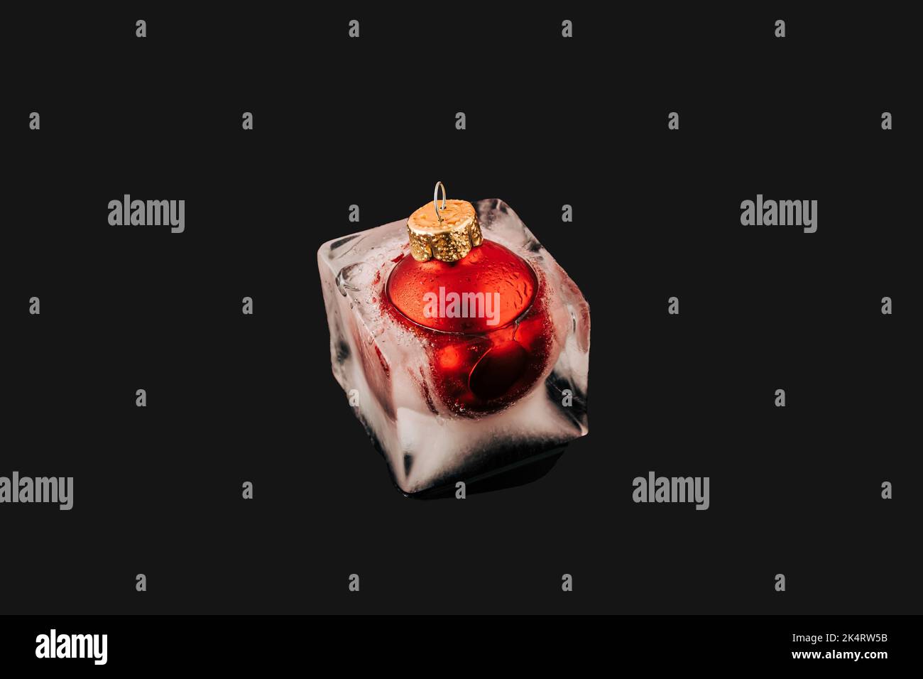 Rote weihnachtskugel Dekoration in schmelzendem Eiswürfel auf schwarzem Hintergrund. Neujahrskarte. Minimalkonzept Stockfoto