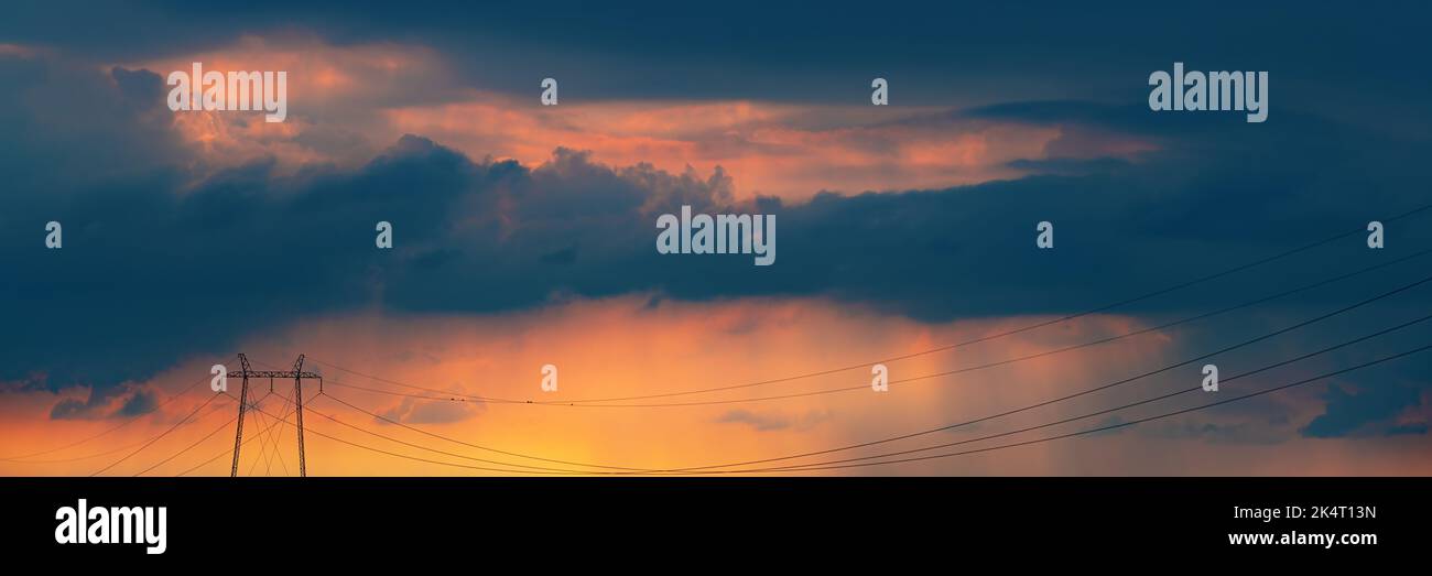 Globales Energiekrisenkonzept, Strommasten im Sendeturm mit Oberleitungskabeln und stürmischen Wolken im Hintergrund, um das zu unterstreichen Stockfoto