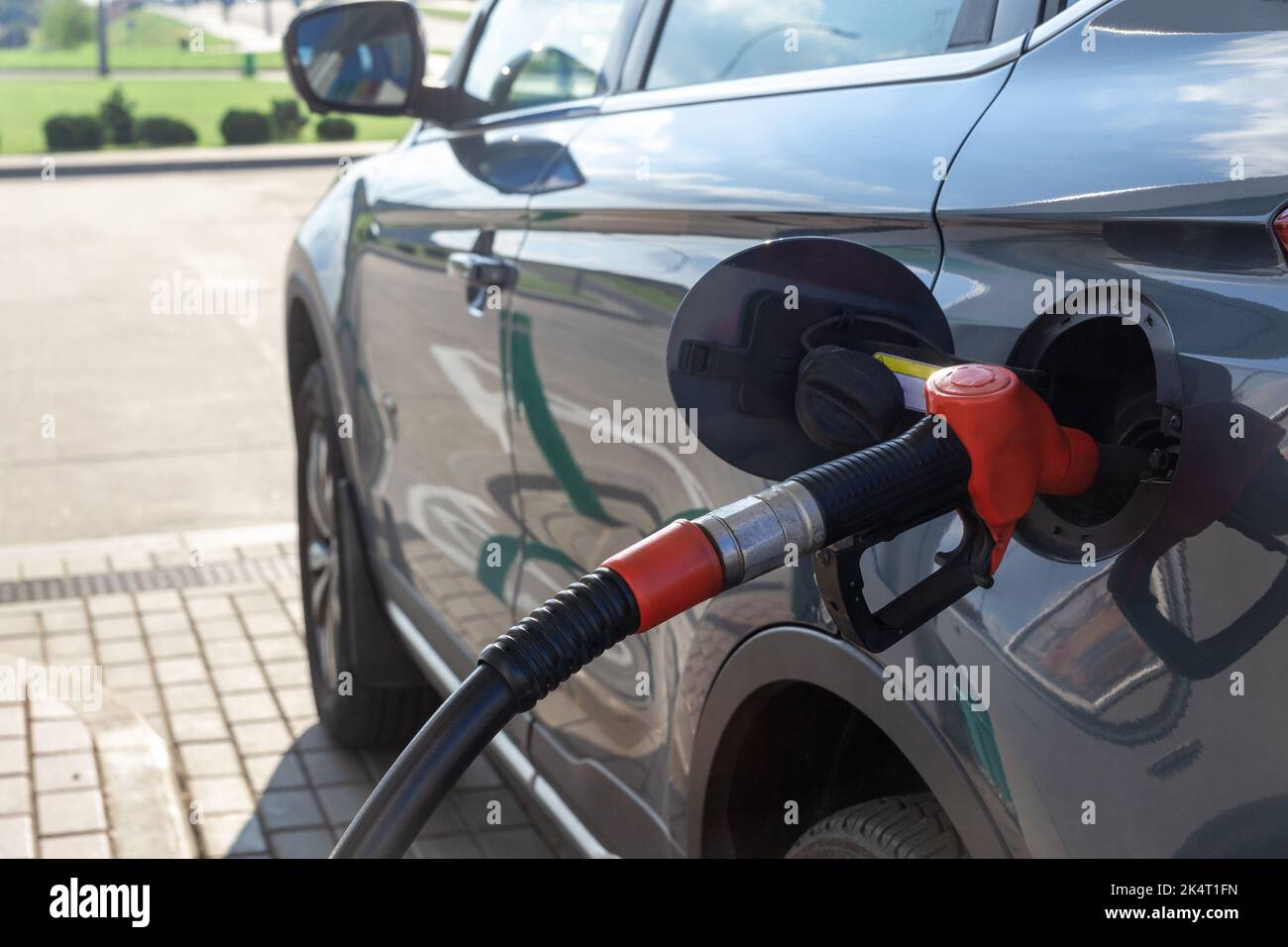 Kraftstoffdüse zum Nachfüllen von Kraftstoff im Auto an der Tankstelle. Roter Kraftstoffverteiler auf grauem Auto in Petro-Station. Stockfoto