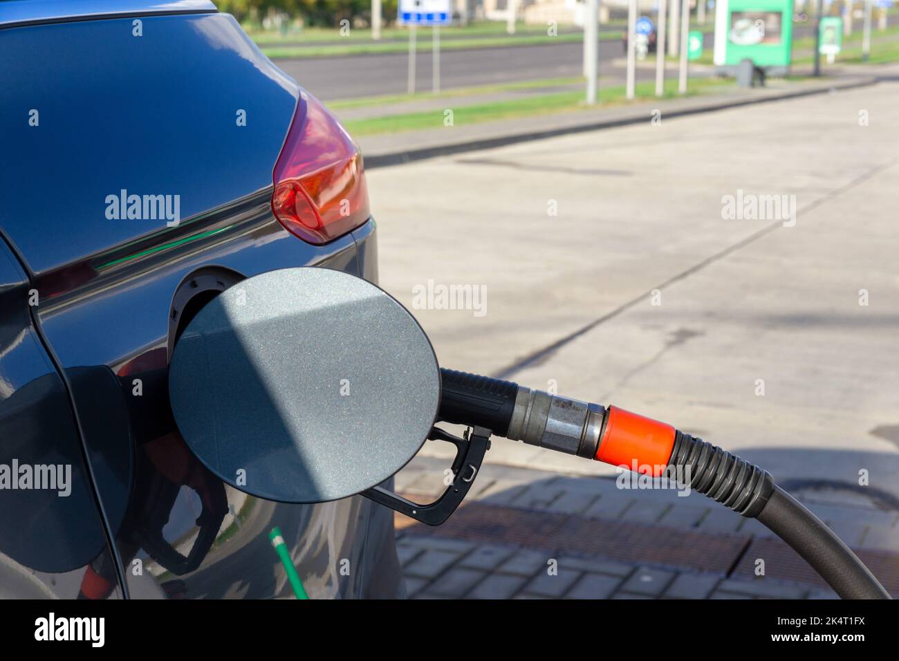 Kraftstoffdüse zum Nachfüllen von Kraftstoff im Auto an der Tankstelle. Roter Kraftstoffverteiler auf grauem Auto in Petro-Station. Stockfoto