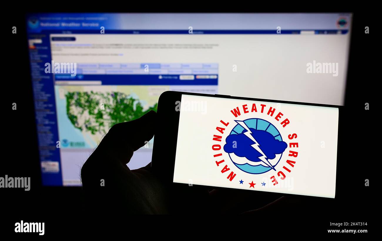Person, die das Smartphone mit dem Logo der US-Agentur National Weather Service (NWS) auf dem Bildschirm vor der Website hält. Konzentrieren Sie sich auf die Telefonanzeige. Stockfoto