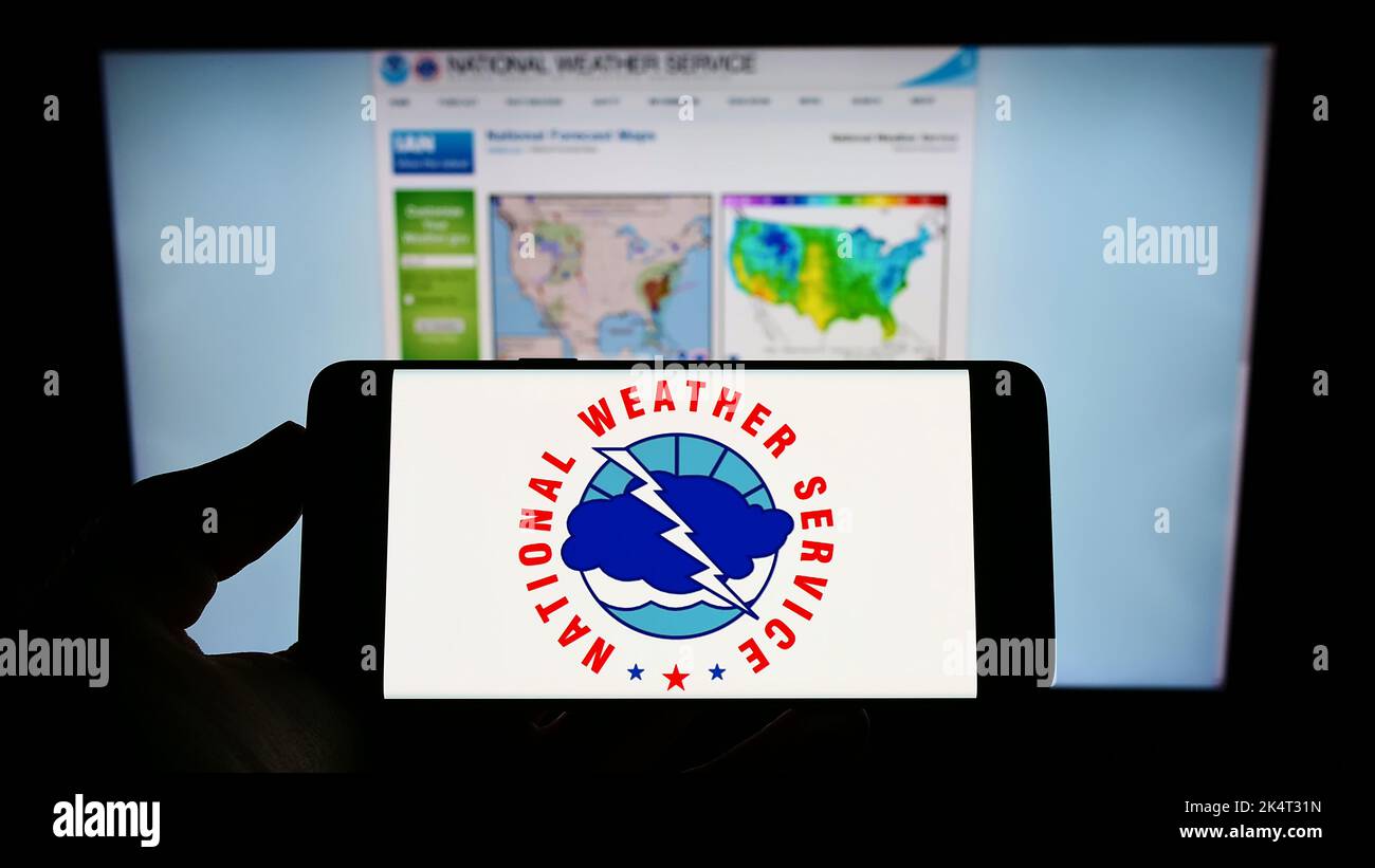 Person, die das Mobiltelefon mit dem Logo der amerikanischen Agentur National Weather Service (NWS) auf dem Bildschirm vor der Webseite hält. Konzentrieren Sie sich auf die Telefonanzeige. Stockfoto