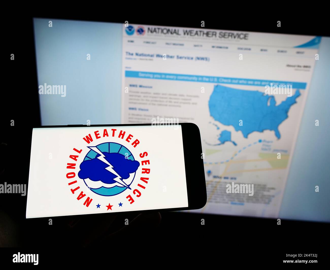 Person, die Mobiltelefon mit dem Logo der US-Agentur National Weather Service (NWS) auf dem Bildschirm vor der Webseite hält. Konzentrieren Sie sich auf die Telefonanzeige. Stockfoto