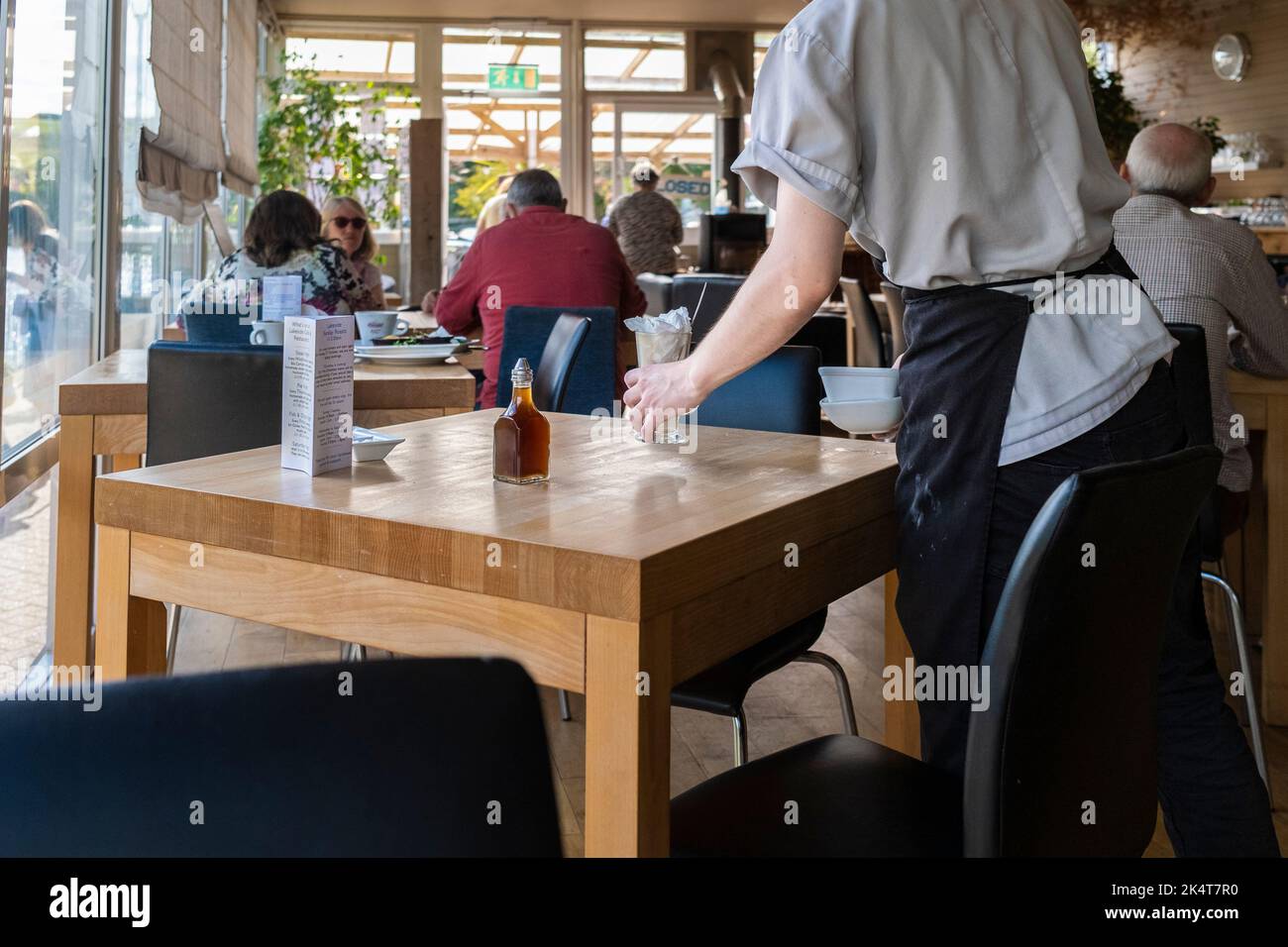 Ein Küchenmitarbeiter, der Tische in einem belebten Restaurant in Newquay in Cornwall im Vereinigten Königreich abräumte. Stockfoto