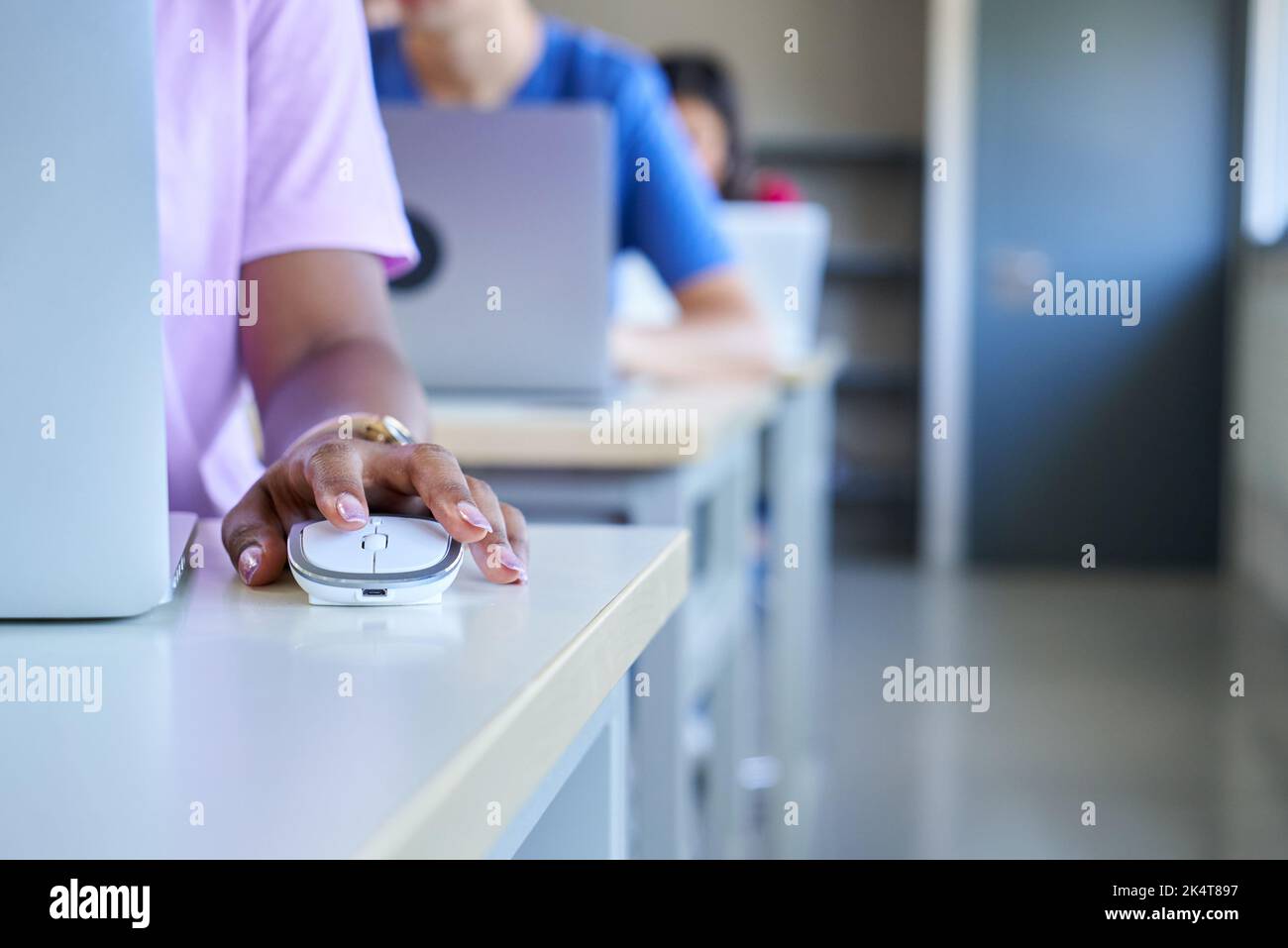 Nahaufnahme der dunklen Haut Hand mit Computer-Maus im Klassenzimmer, unkenntlich Mädchen und Kollegen. Stockfoto