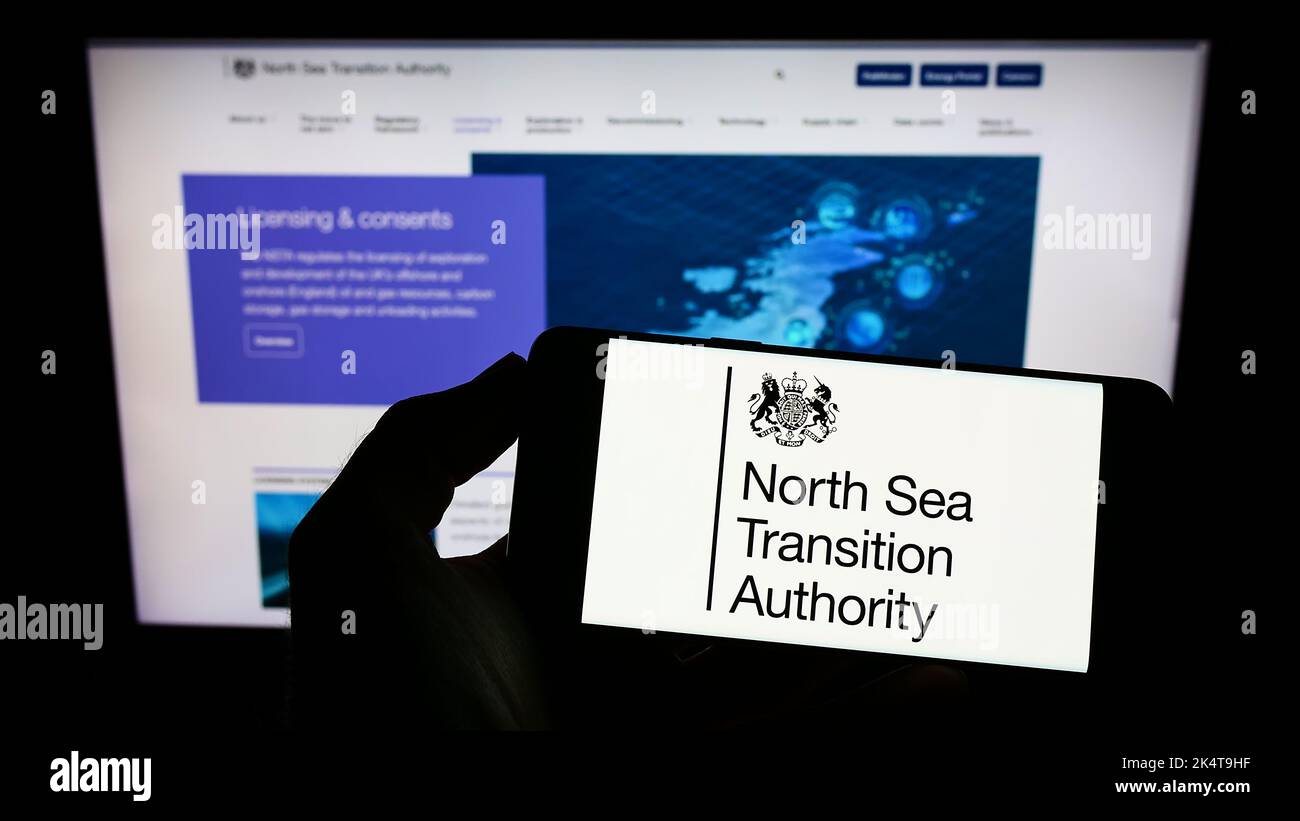 Person mit Mobiltelefon und Logo der britischen North Sea Transition Authority (NSTA) auf dem Bildschirm vor der Webseite. Konzentrieren Sie sich auf die Telefonanzeige. Stockfoto