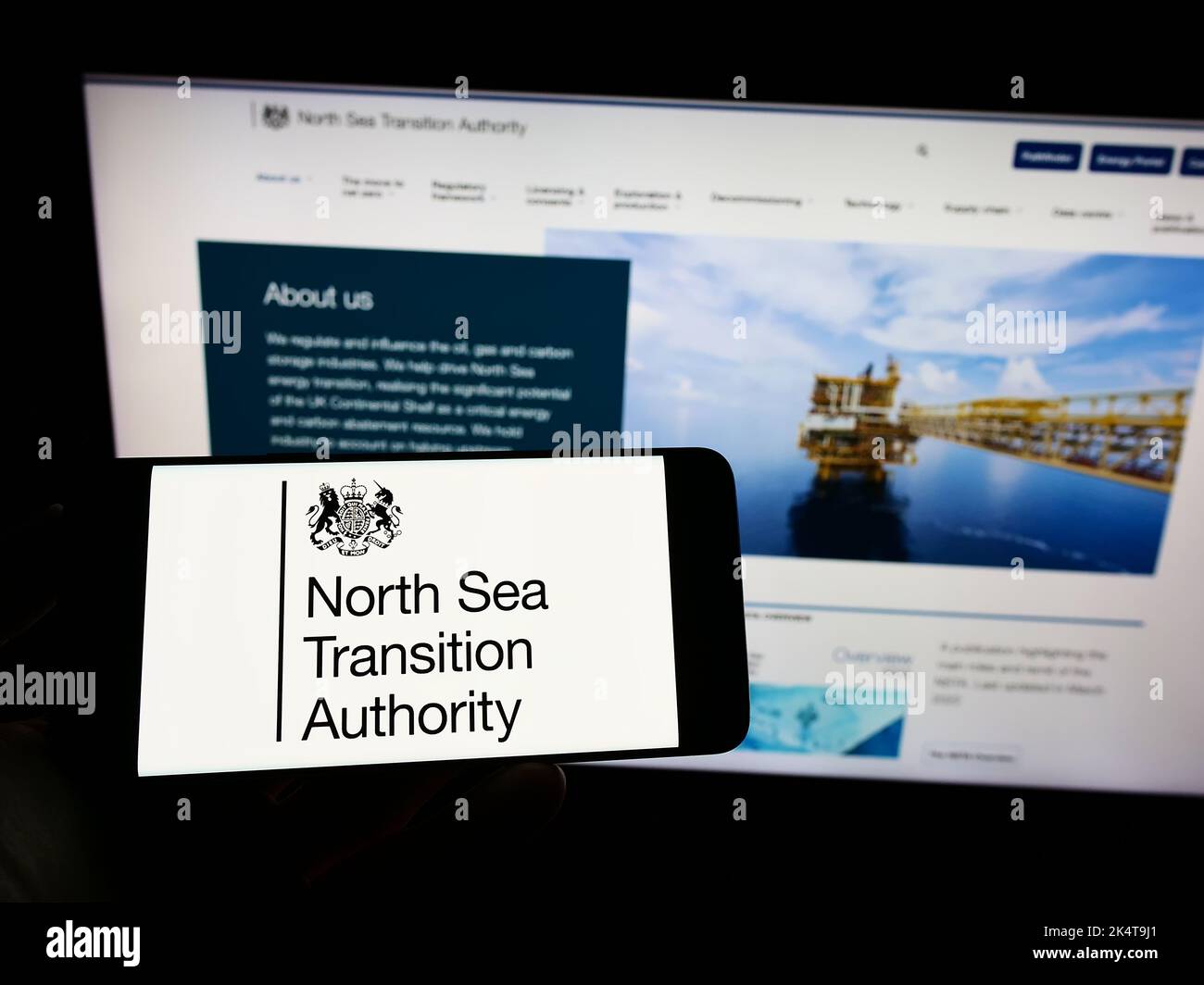 Person mit Mobiltelefon und Logo der britischen North Sea Transition Authority (NSTA) auf dem Bildschirm vor der Webseite. Konzentrieren Sie sich auf die Telefonanzeige. Stockfoto