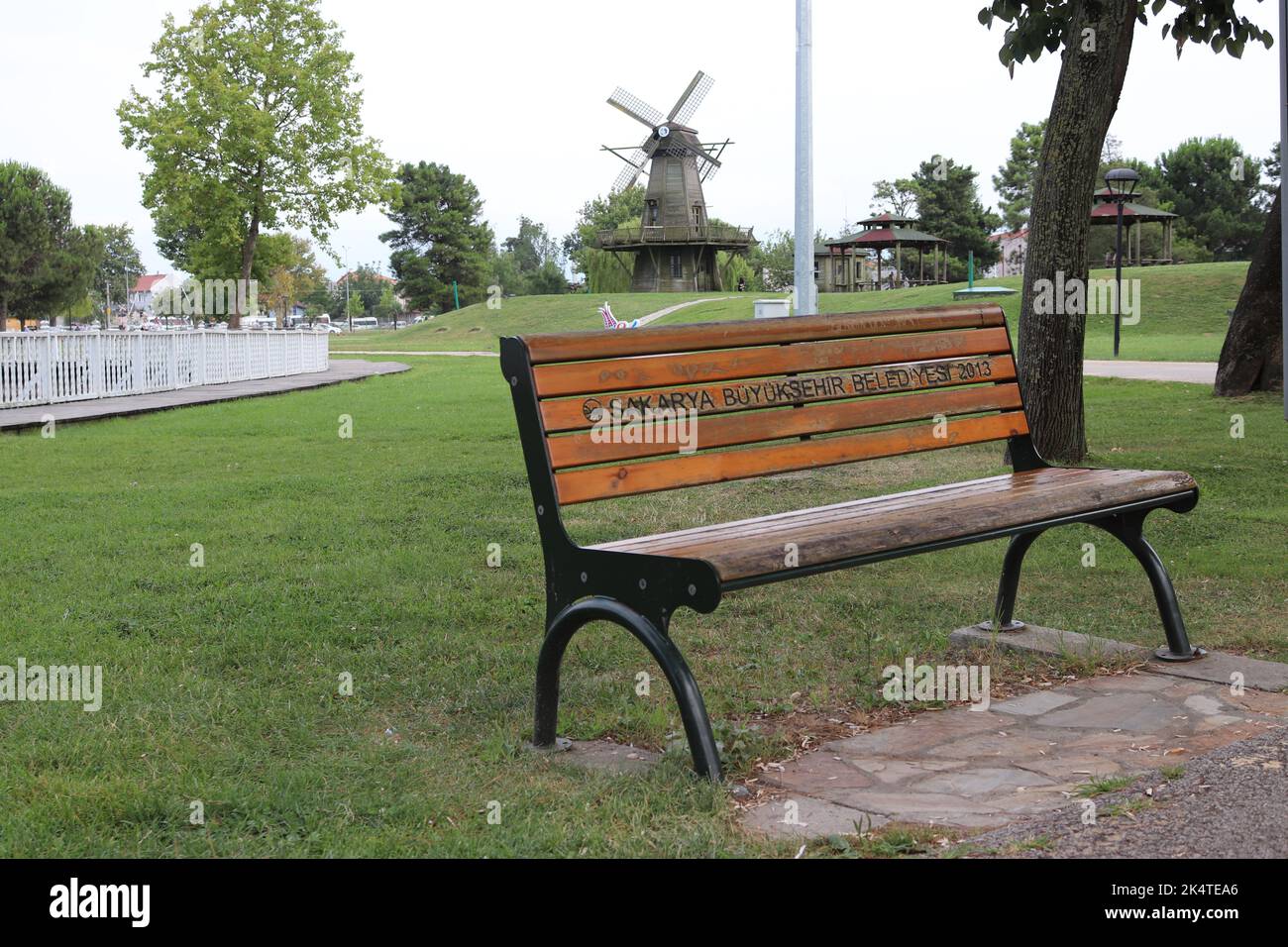 Sakarya City Park (türkisch: Sakarya Kent Park ), Parkbank. Leere Parkbank. Windmühle im Hintergrund. Sakarya ist eine Stadt in der Türkei. Übersetzung von Stockfoto