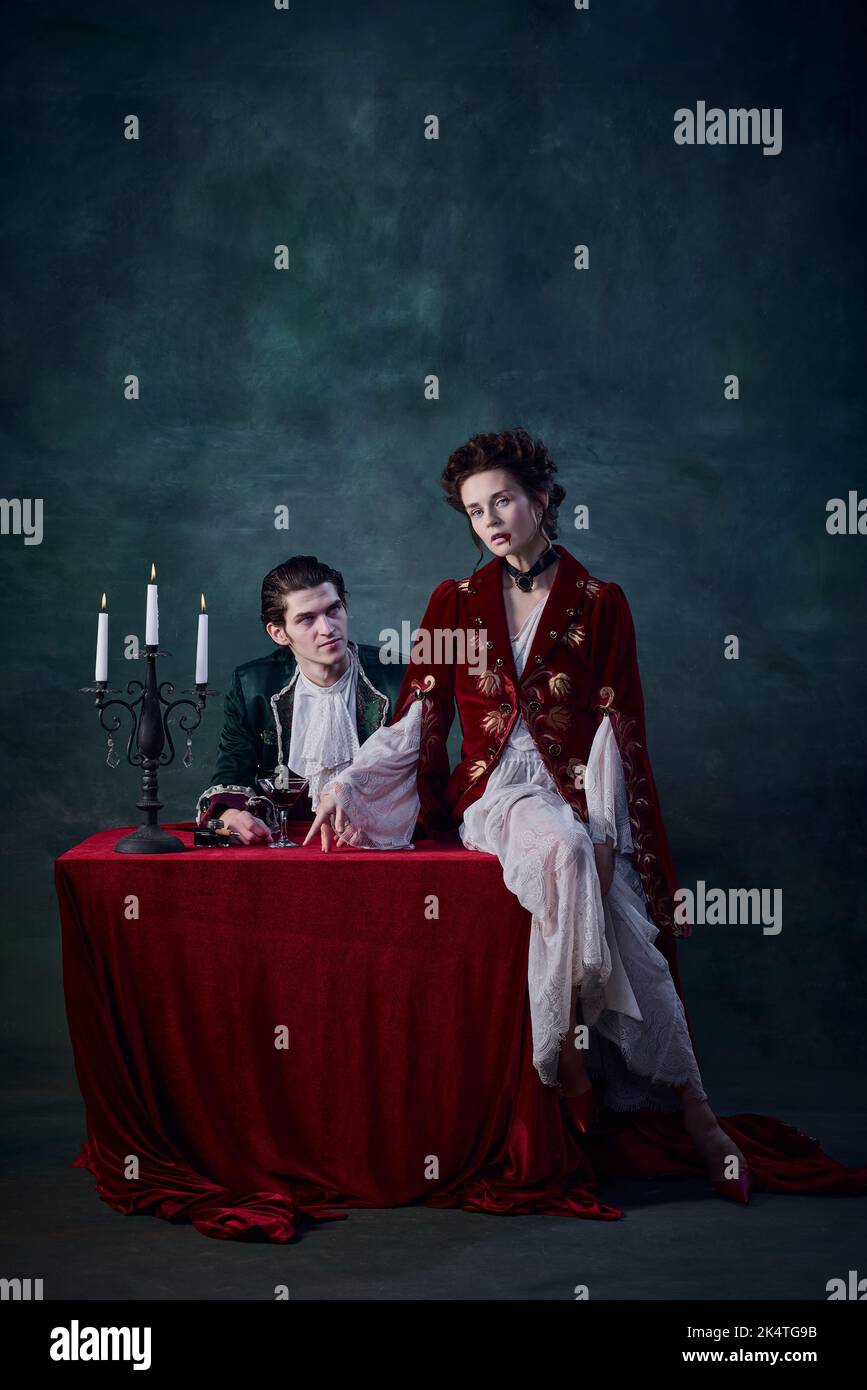 Portrait von phantastischer Frau und Mann, Vampire in mittelalterlichen Kostümen auf dunkelgrünem Hintergrund. Bluttrinken Stockfoto