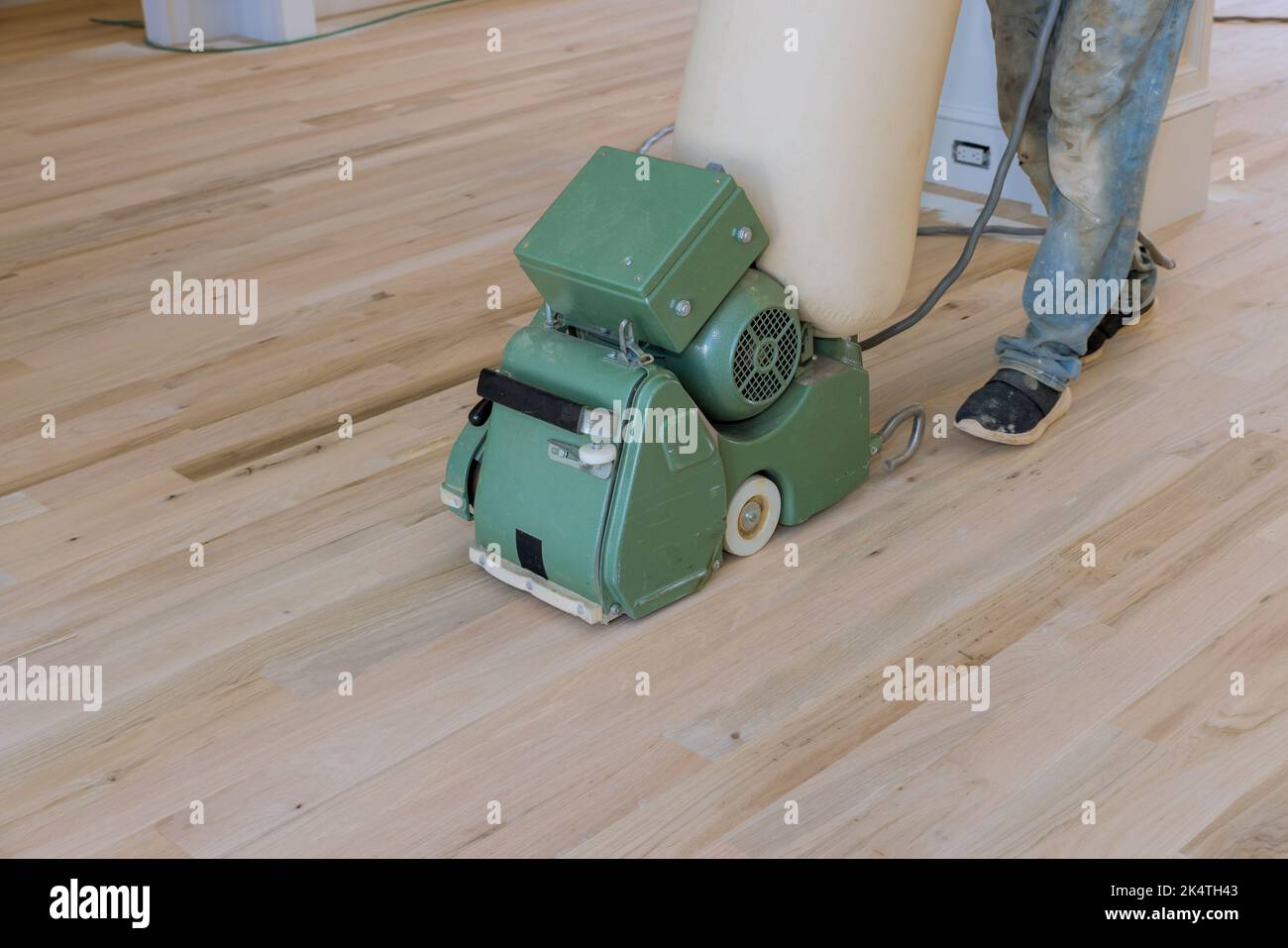 Mit einem Bodenschleifer mahlt ein neuer Hausbesitzer in einem neu errichteten Haus einen Holzparkettboden, wobei das Schleifrad als Werkzeug verwendet wird Stockfoto