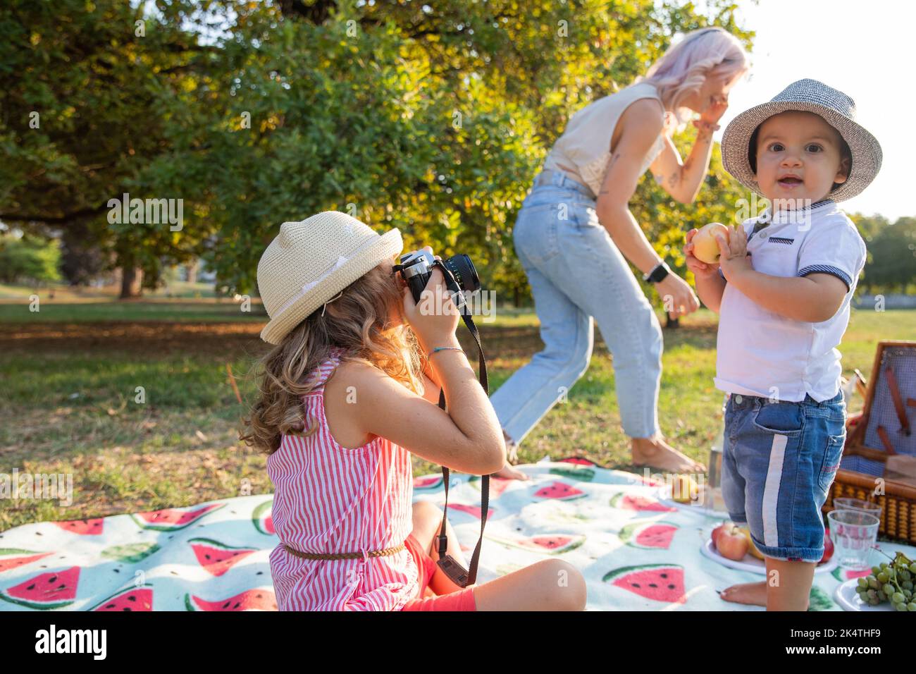 Baby Mädchen macht Fotos von Baby-Bruder mit Analogkamera, während Mama telefoniert während Picknick. Stockfoto
