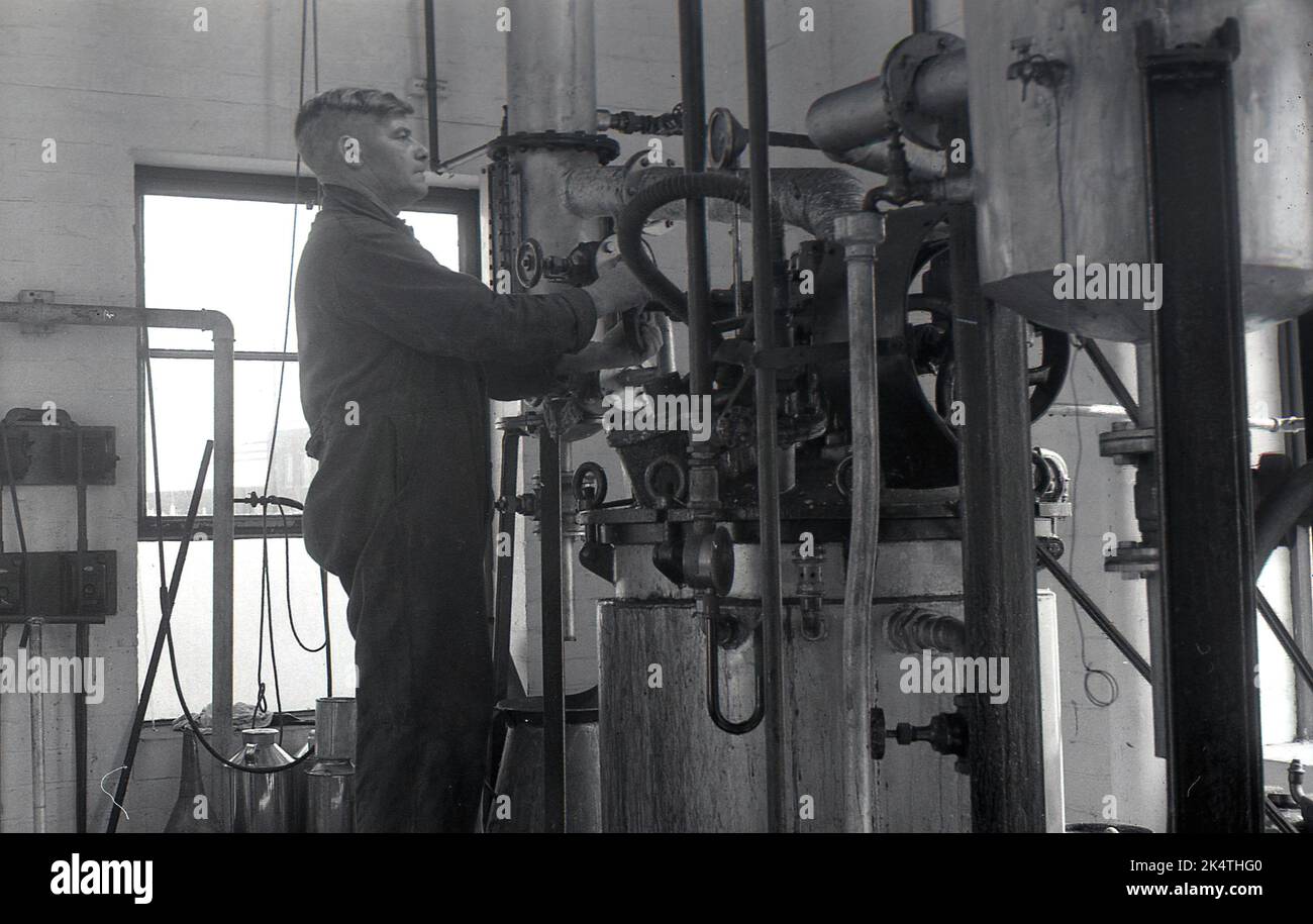 1960er Jahre, ein Bediener, der an den Rohrleitungen auf einer erhöhten Plattform in einer Industrieeinheit in einer kleinen Lackiererei arbeitet. Stockfoto