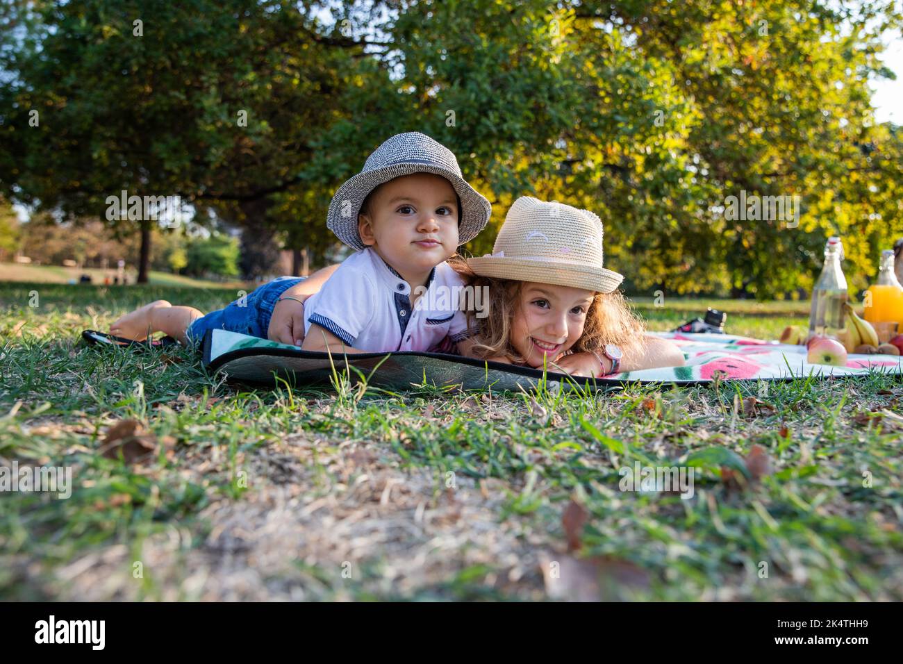 Zwei schöne und fröhliche Kinder, die auf der Picknickmatte liegen, blicken amüsiert nach vorne. Stockfoto