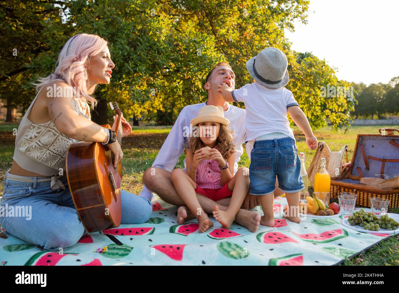 Vierköpfige Familie mit Mama, die Gitarre spielt, beim Picknick im Park. Stockfoto