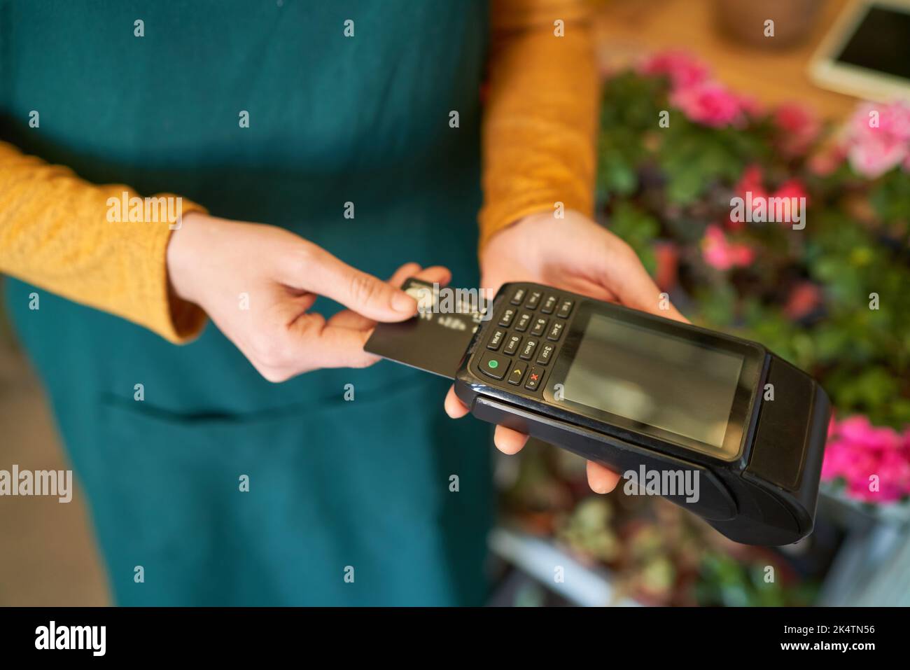 Die Hand hält die Kreditkarte während der mobilen Zahlung im Einzelhandel im Blumenladen dem Leser Stockfoto