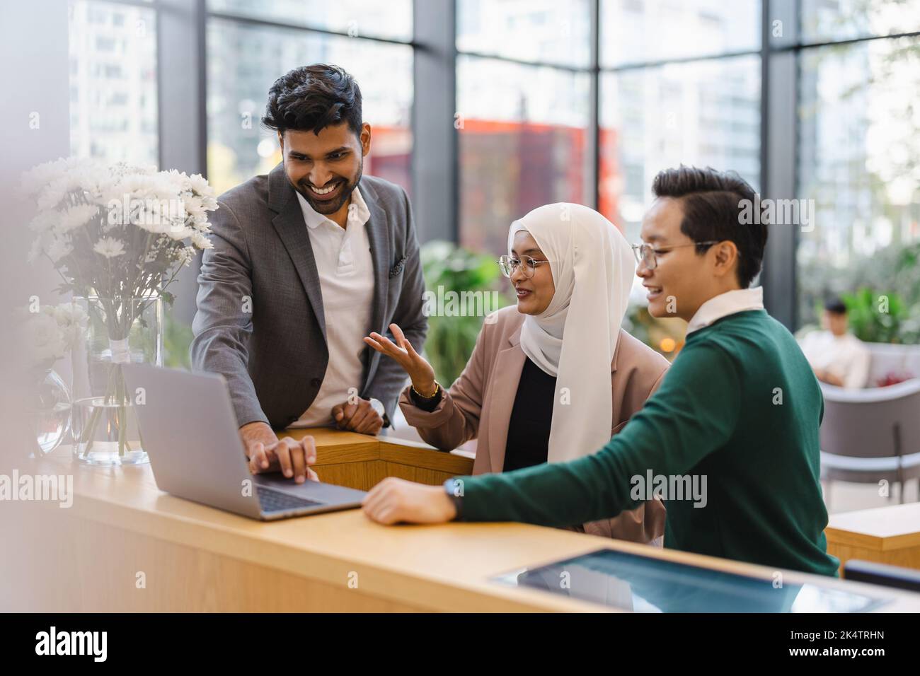 In einem modernen Büro versammeln sich zahlreiche Geschäftsleute um einen Laptop Stockfoto