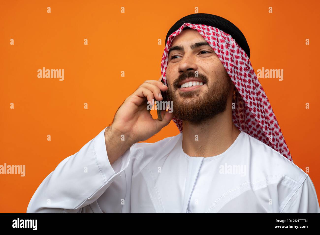 Arabischer Geschäftsmann im Gespräch auf Handy vor orangenen Hintergrund Stockfoto