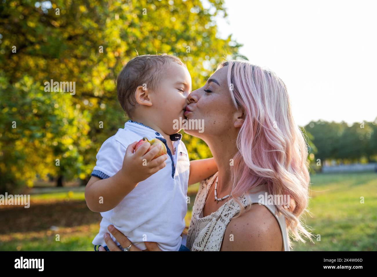Während eines Spaziergangs im Park küsst Mutter ihr Baby zärtlich auf den Mund. Stockfoto