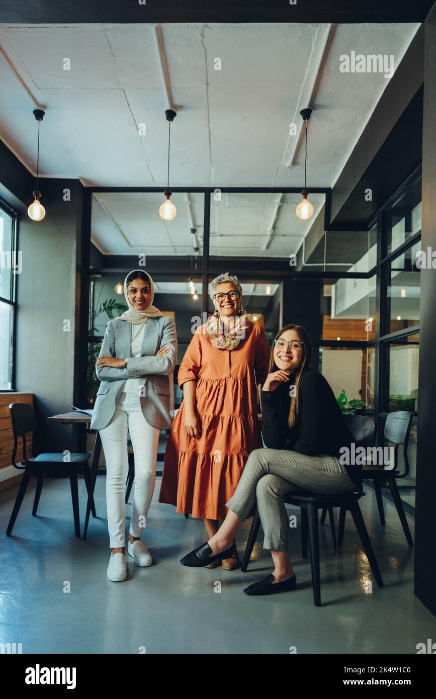 Drei verschiedene Geschäftsfrauen lächeln in einem Büro an der Kamera. Gruppe multikultureller Unternehmer, die als Team an einem integrativen Arbeitsplatz arbeiten. Nachf. Stockfoto