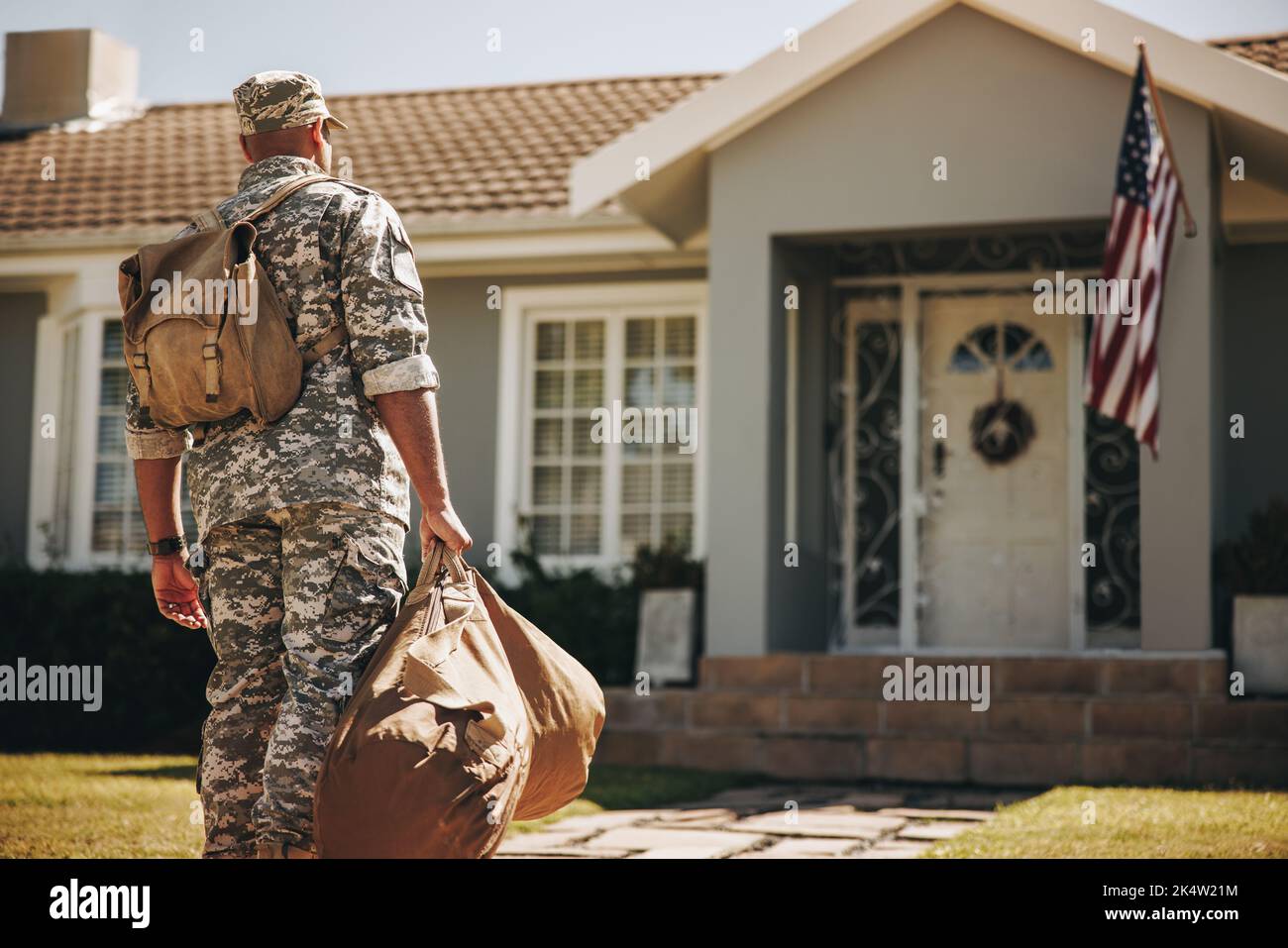 Rückansicht eines mutigen jungen Soldaten, der mit seinem Gepäck auf sein Haus zuläuft. Amerikanischer Militärangehöriger, der nach seinem Dienst in seinem Land nach Hause zurückkehrt Stockfoto