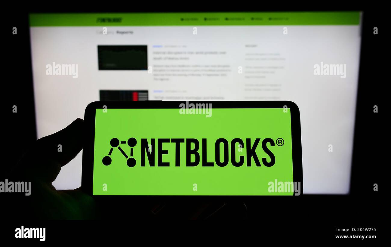 Person, die Mobiltelefon mit dem Logo des Internet Watchdog NetBlocks Ltd. Auf dem Bildschirm vor der Webseite hält. Konzentrieren Sie sich auf die Telefonanzeige. Stockfoto