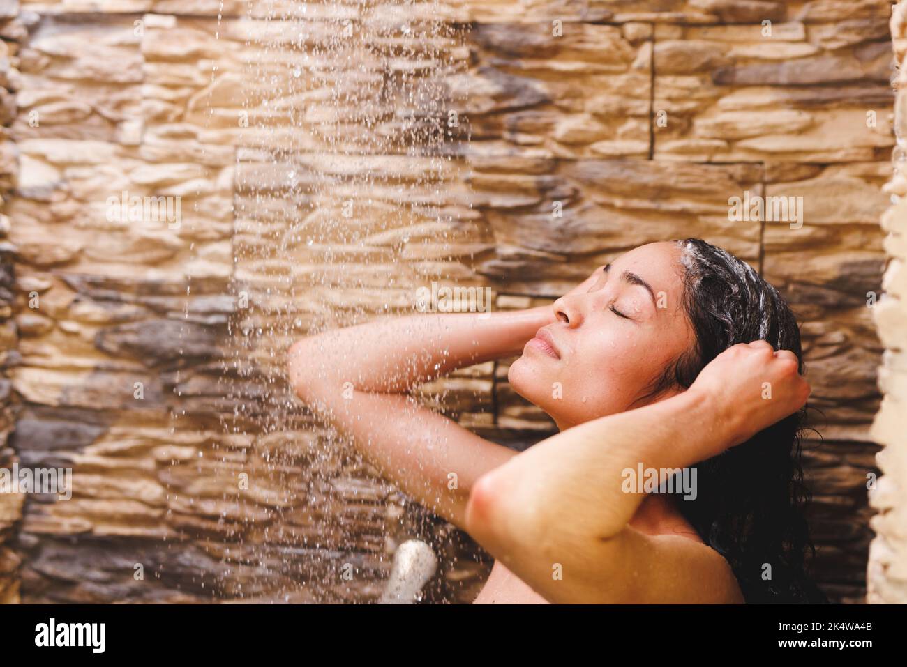 Glückliche Birazialfrau, die duscht und im Badezimmer Haare wäscht Stockfoto