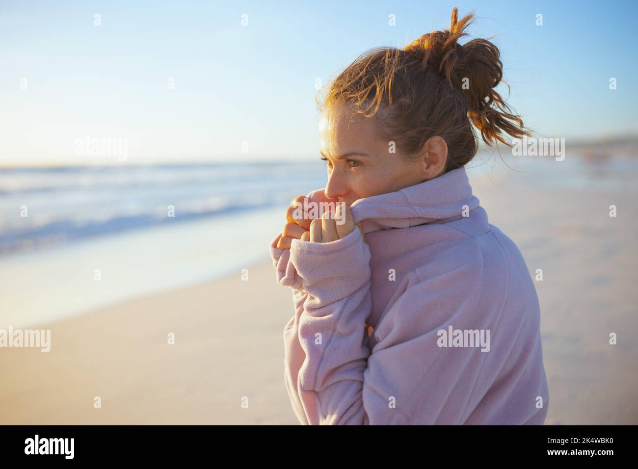 Elegante 40-jährige Frau in kuscheligem Pullover am Strand am Abend entspannend. Stockfoto